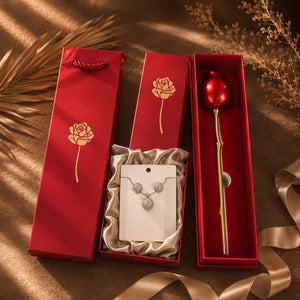 A gift set containing a red rose-shaped stem with a red top and gold stem, alongside a silver necklace with a matching pendant, all presented in red gift boxes with gold rose illustrations on a brown satin background.
